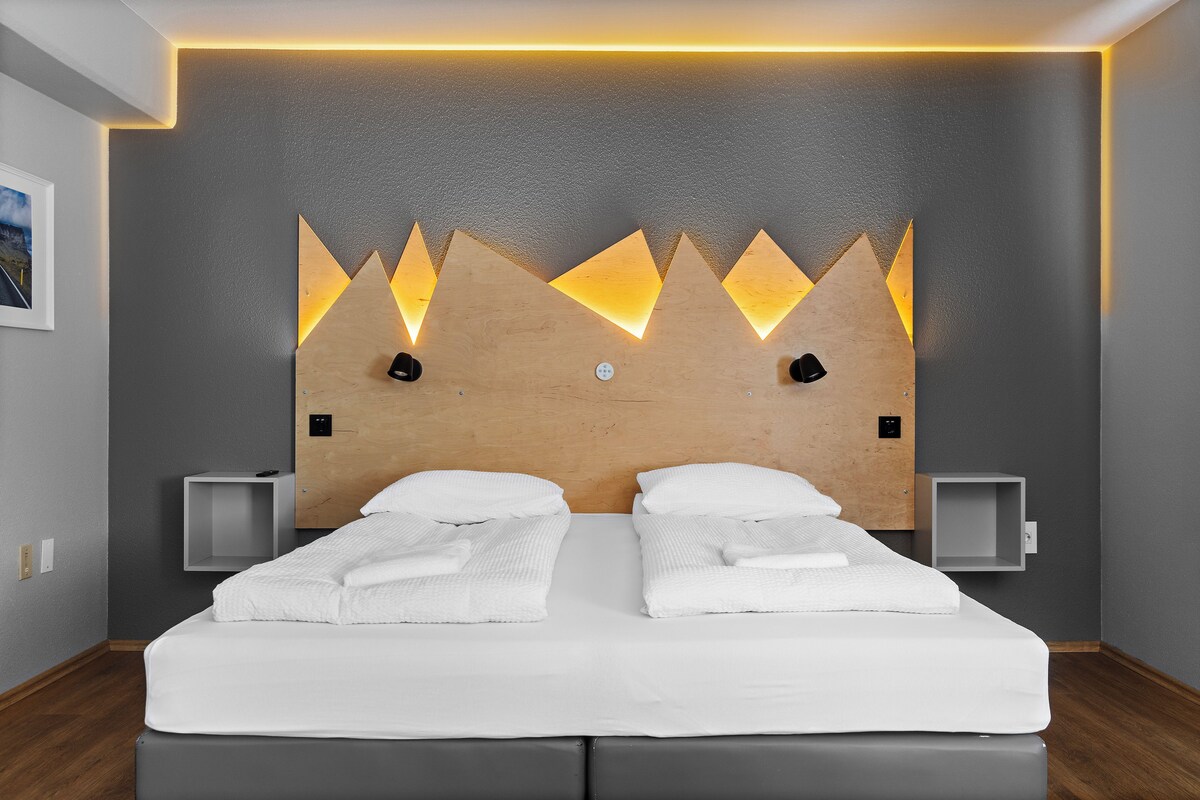 A modern hotel room with a large bed, two bedside tables, and a unique wall design with triangular light fixtures.