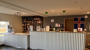A reception area with a check-in counter, a wall clock, and a flag. - Start Hostel (Reykjanesbær)