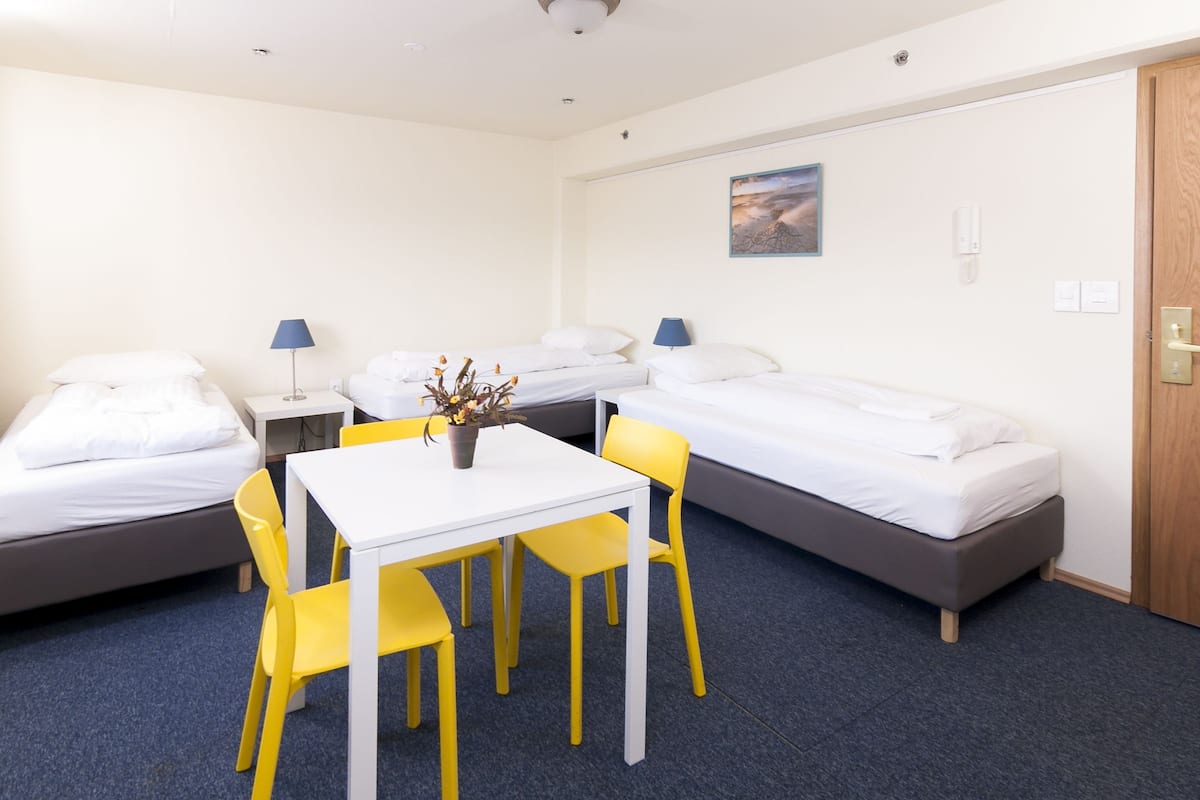 A hotel room with two single beds, a small table with chairs, a desk, and a lamp.