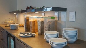 A buffet setup with stacked plates and bowls, a food dispenser, and a condiment station. - Start Hostel (Reykjanesbær)