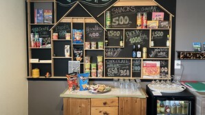 A kiosk with various snacks and drinks, including chips, pasta, noodles, and beverages, displayed on a chalkboard wall. - Start Hostel (Reykjanesbær)