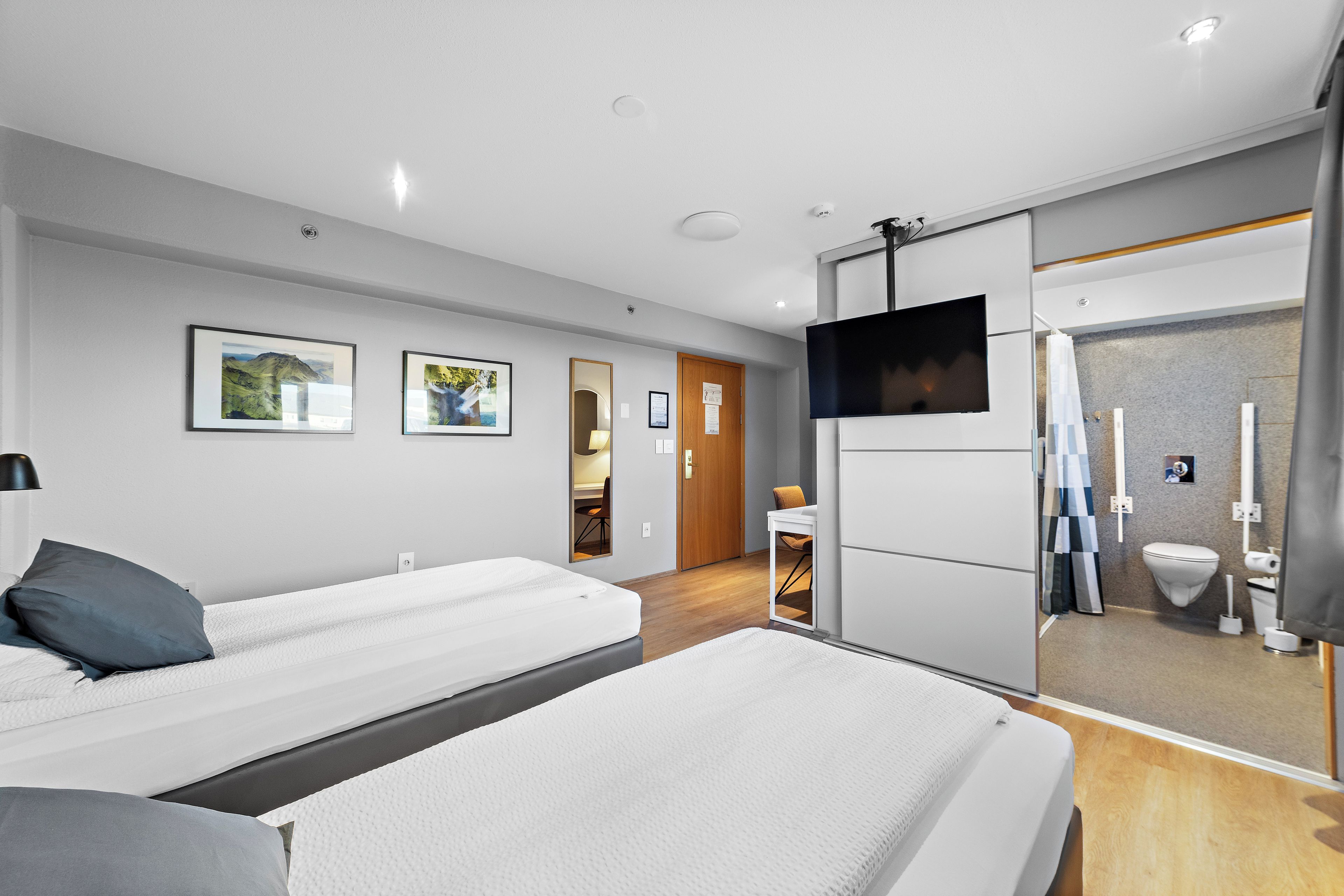 Una habitación de hotel moderna con dos camas, televisión y baño con cortina de ducha.