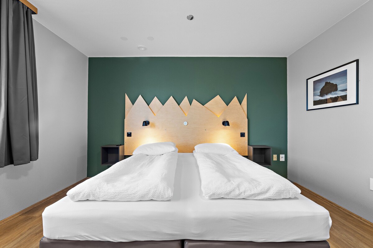 A hotel room with a bed, a headboard, a wall-mounted picture, and a window with curtains.