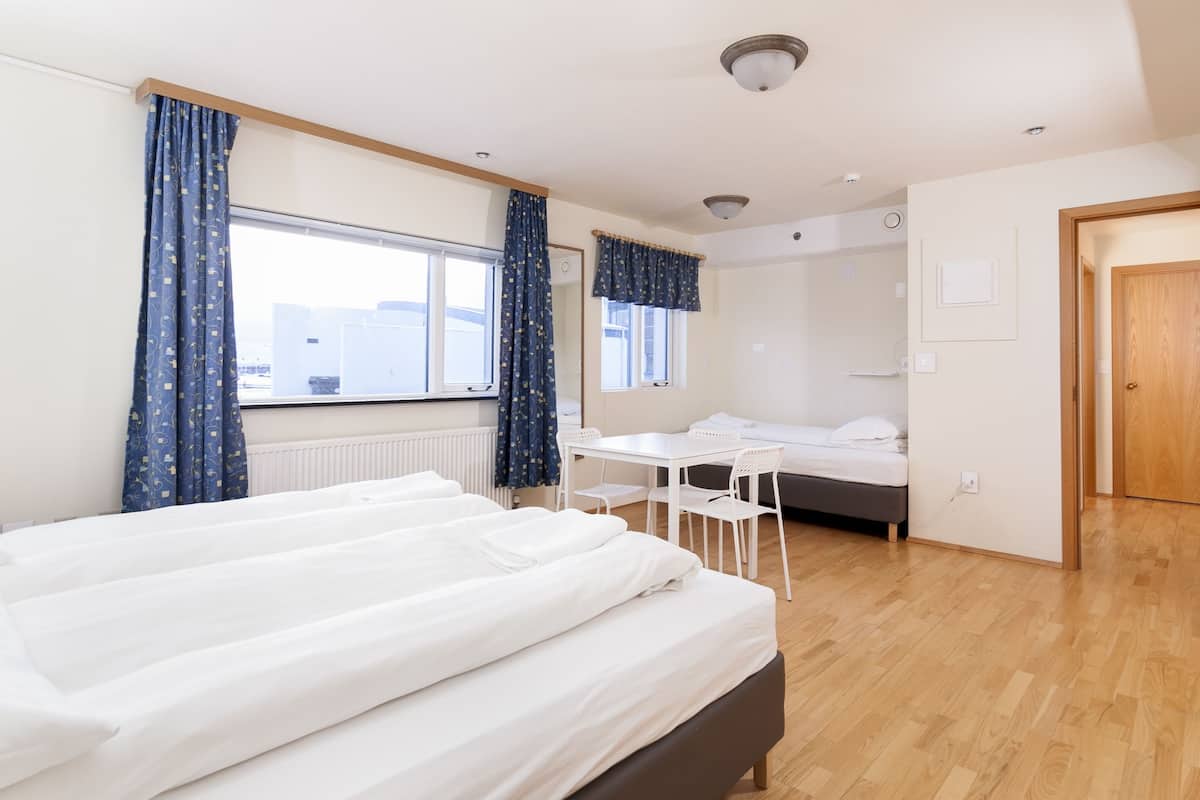 A hotel room with a bed, a small table, a chair, a window, and a door.