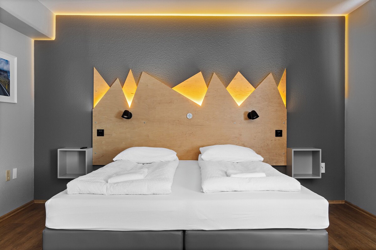 A modern hotel room with a large bed, two bedside tables, and a unique wall design with triangular light fixtures.