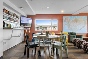 A modern living room with a dining area, a television mounted on the wall, and a large window providing a view of the outdoors. - Start Hostel (Reykjanesbær)