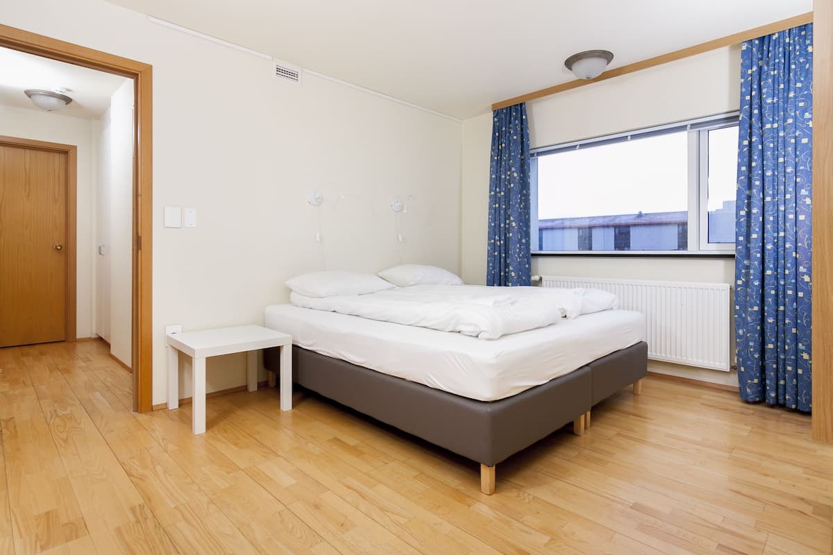A bedroom with a bed, a bedside table, a window with curtains, and a radiator.