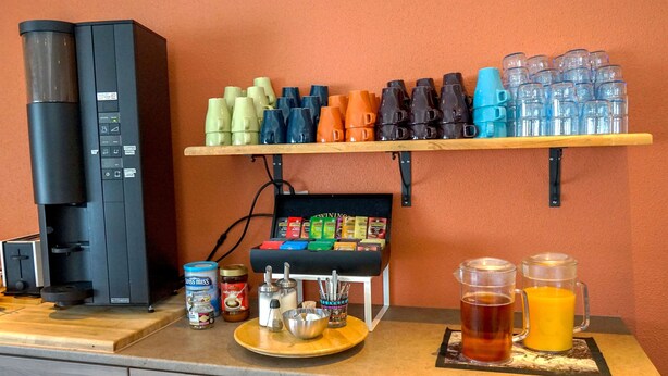 A coffee station with a coffee maker, a variety of coffee cups, a coffee grinder, and a selection of coffee pods. - Start Hostel (Reykjanesbær)