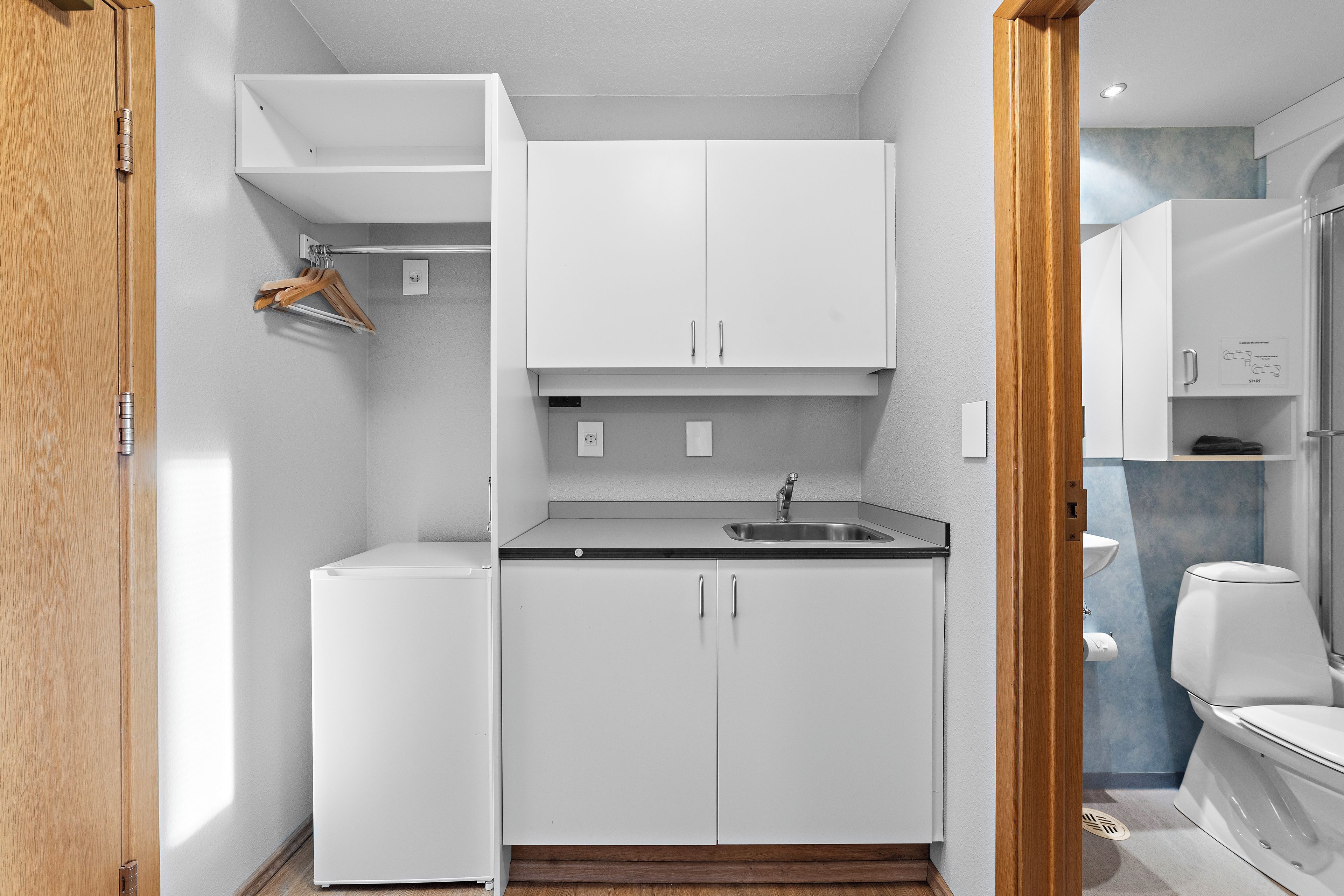 Una cocina compacta con muebles blancos, un lavamanos integrado y un refrigerador pequeño.