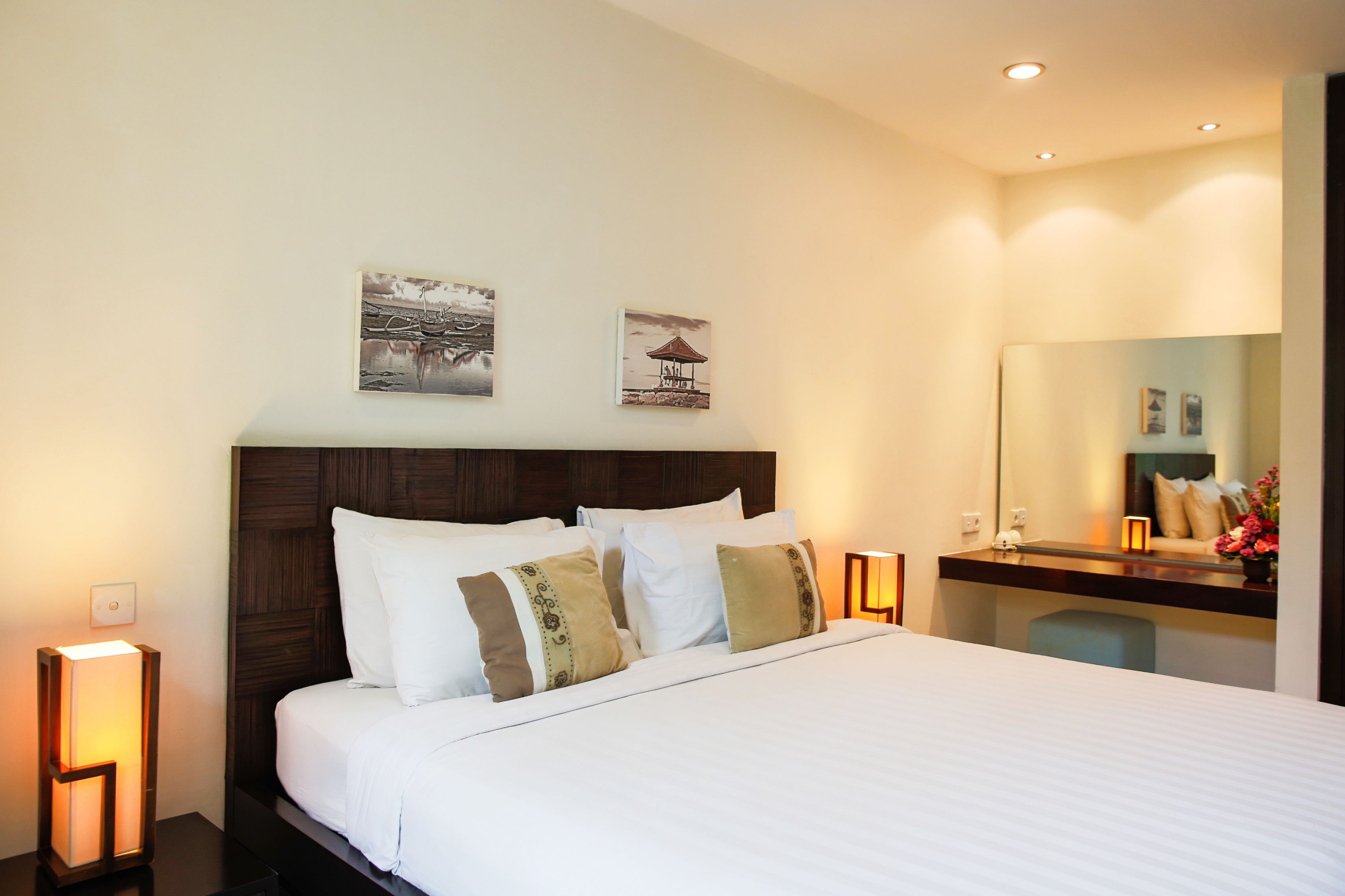 A neatly made bed with white linens and decorative pillows, a wooden headboard, and two wall-mounted artworks depicting serene landscapes.