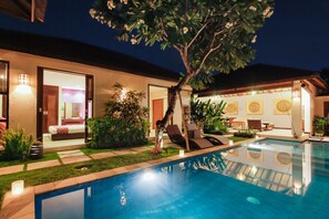 A swimming pool with a sun lounger, a small garden area, and a bedroom visible through an open door. - Samana Villas (Legian)