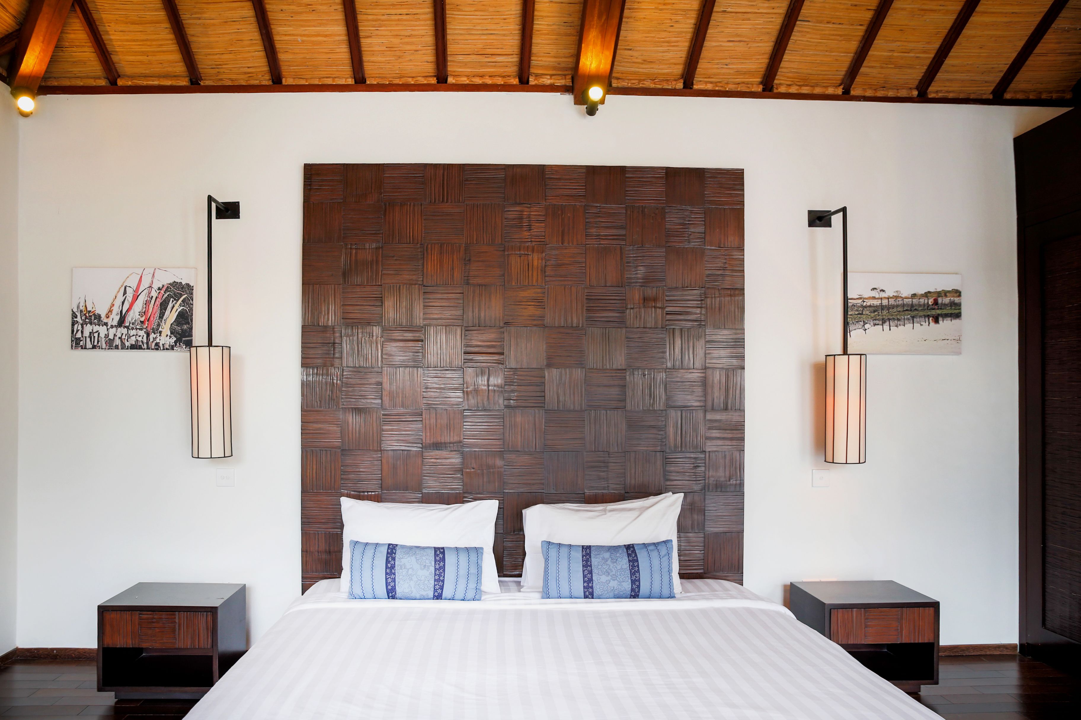 A bedroom with a large bed, wooden headboard, two bedside tables, and wall-mounted lamps.