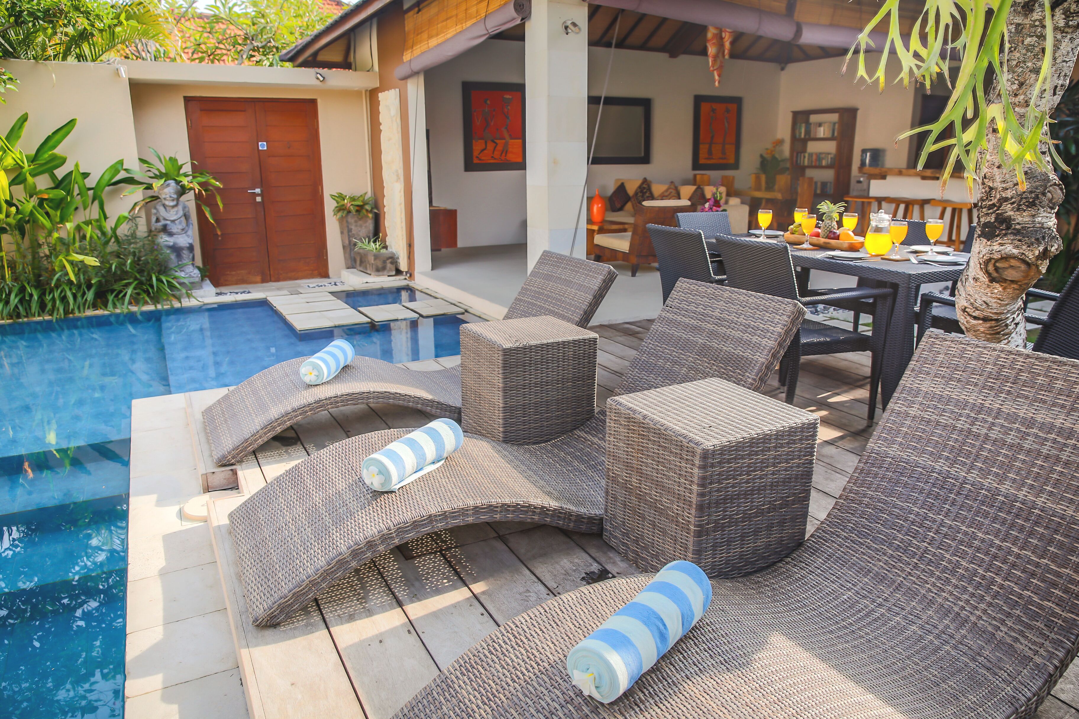A poolside area with wicker lounge chairs and a dining table set for two, overlooking a swimming pool.
