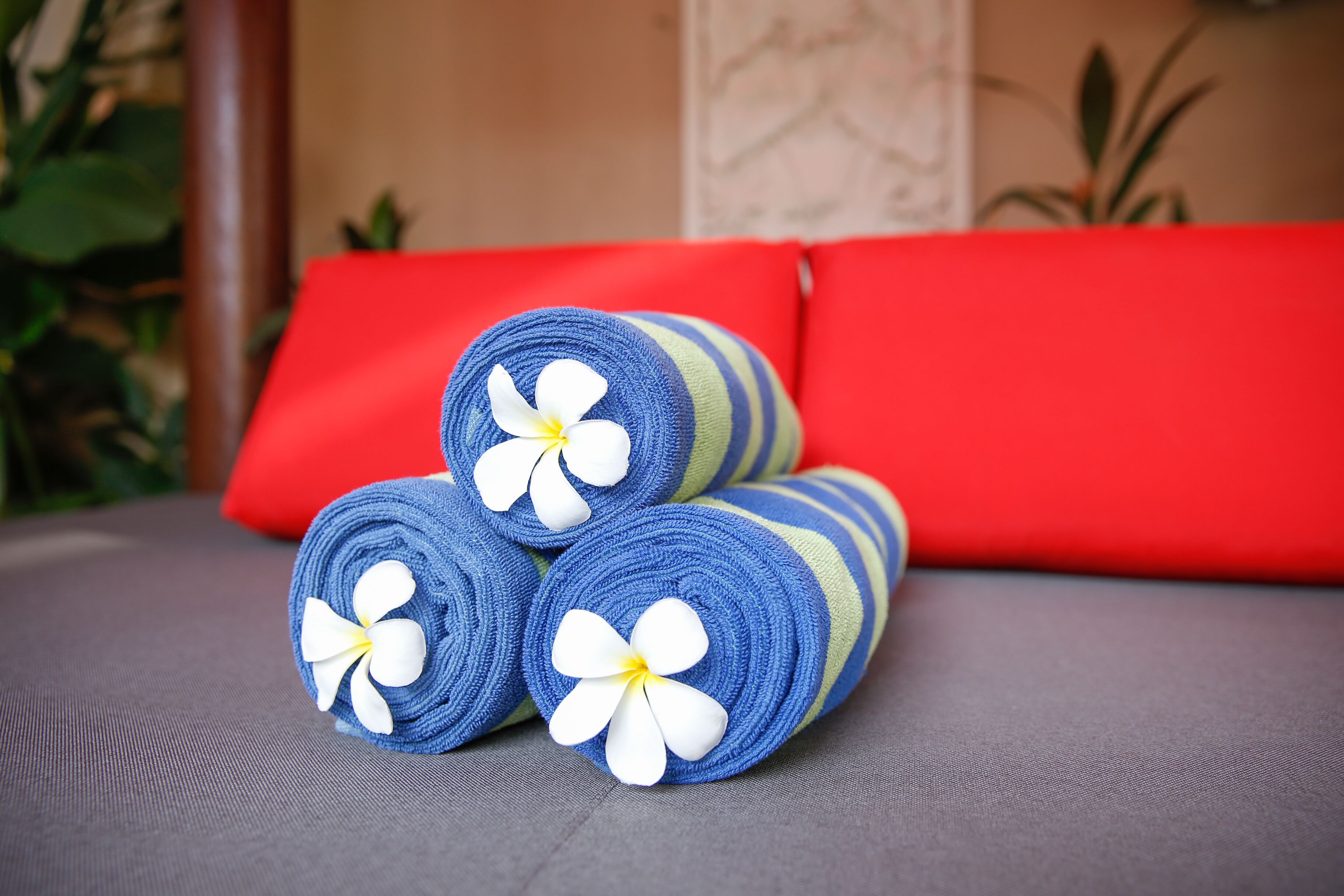 Ein Bett mit roten Kissen und blauen Handtüchern mit weißen Blüten.