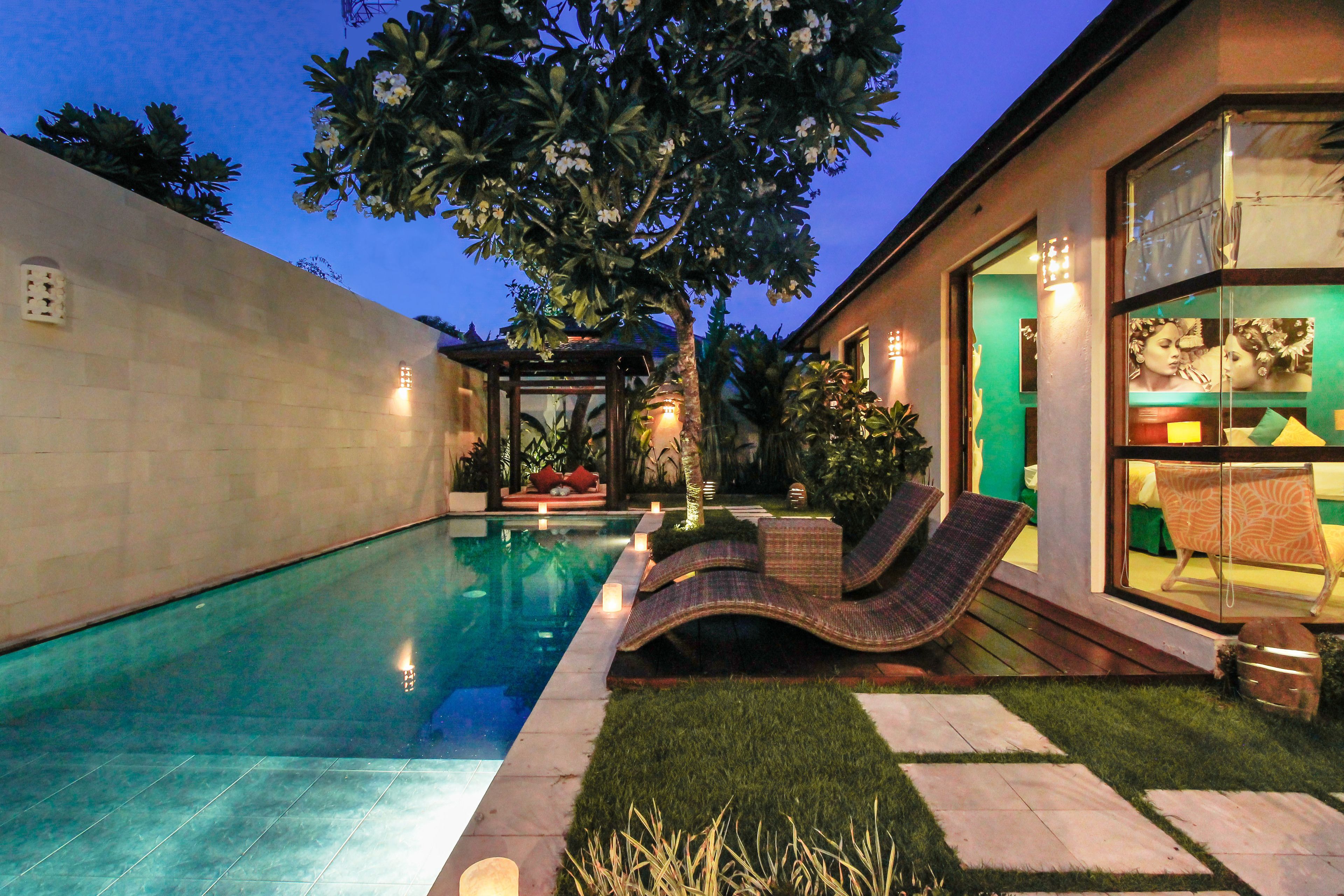 Une piscine avec des chaises longues, un petit jardin et un bâtiment doté de grandes fenêtres.