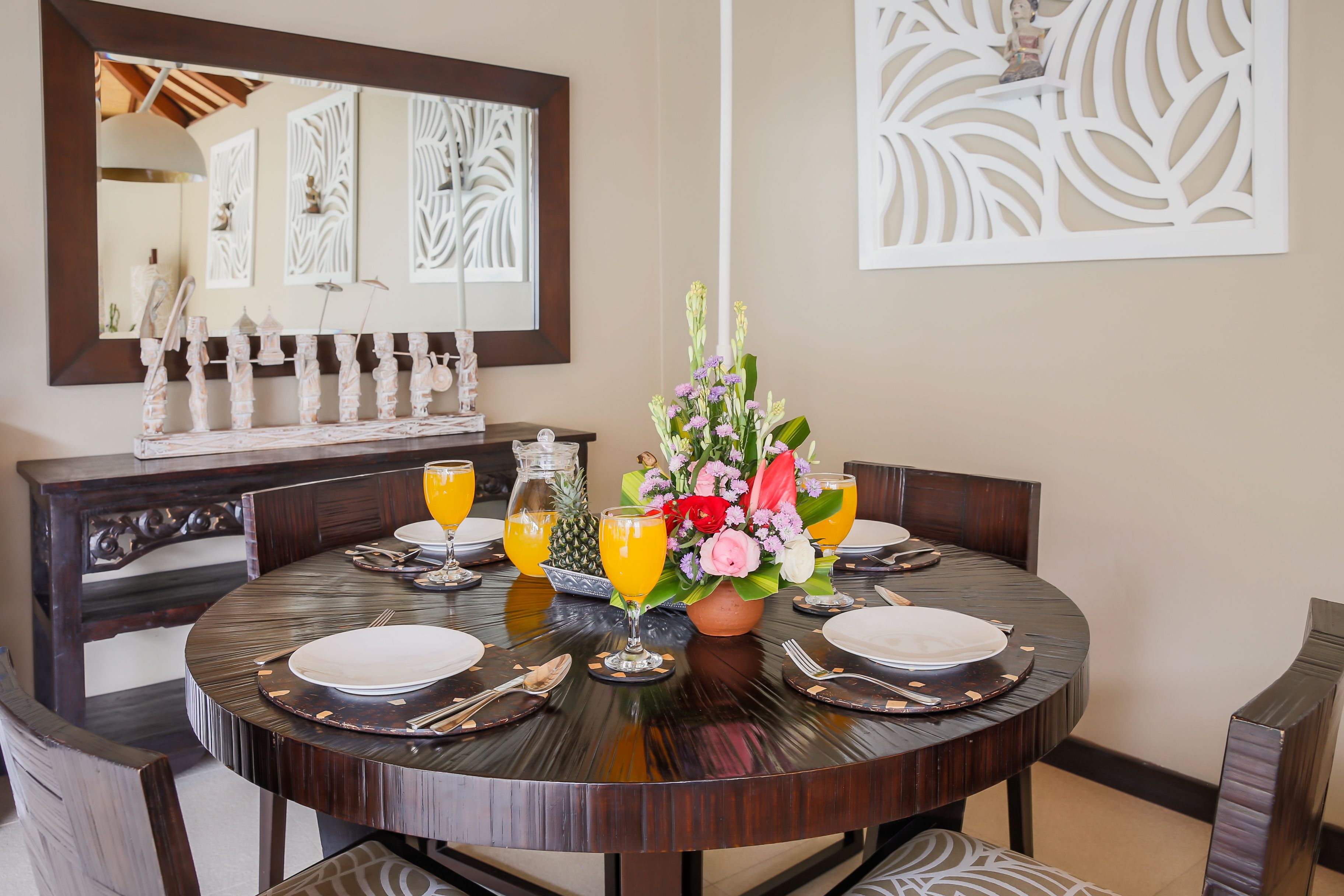 A round dining table set with plates, cutlery, and a centerpiece of flowers and fruit.