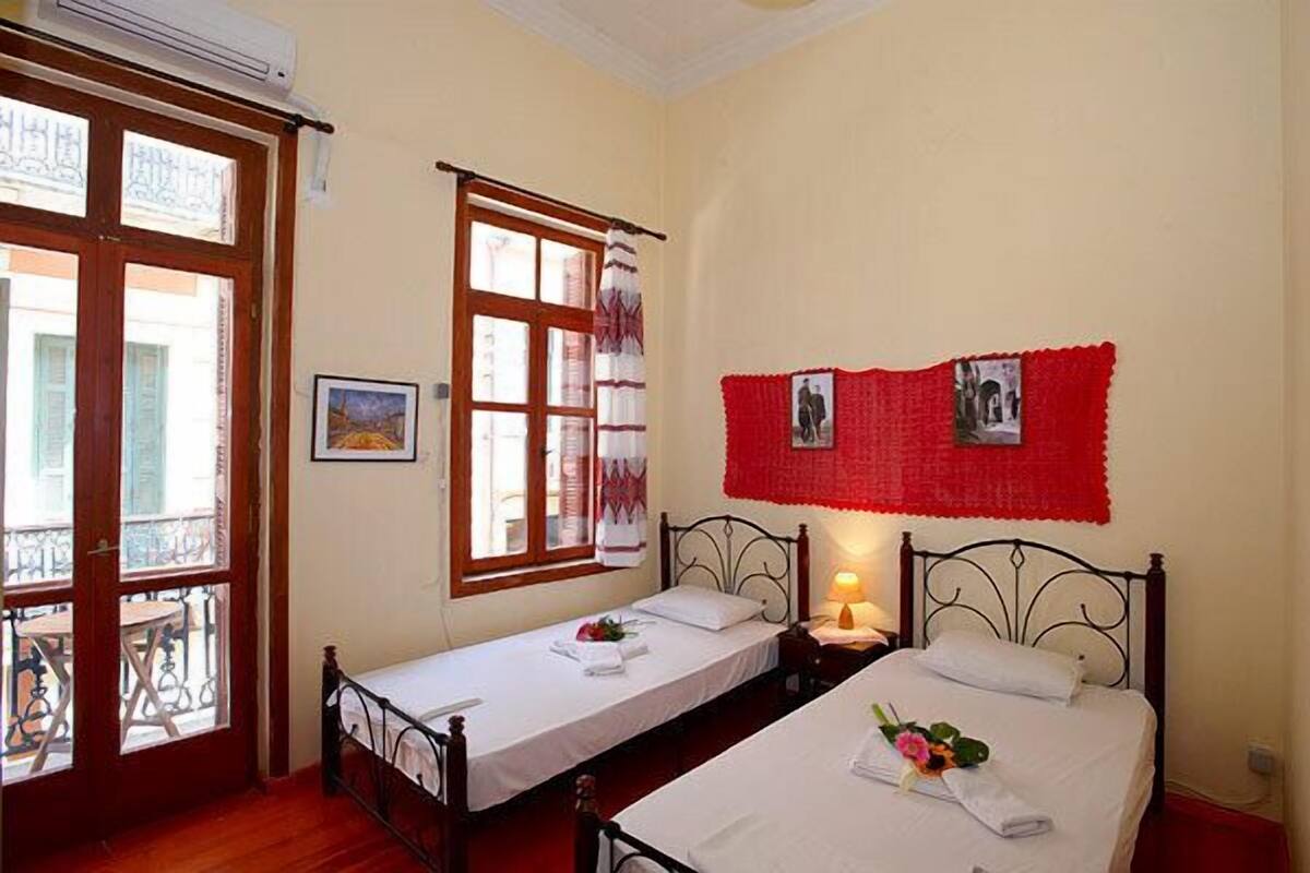Une chambre avec deux lits simples, un balcon et une fenêtre avec des rideaux.