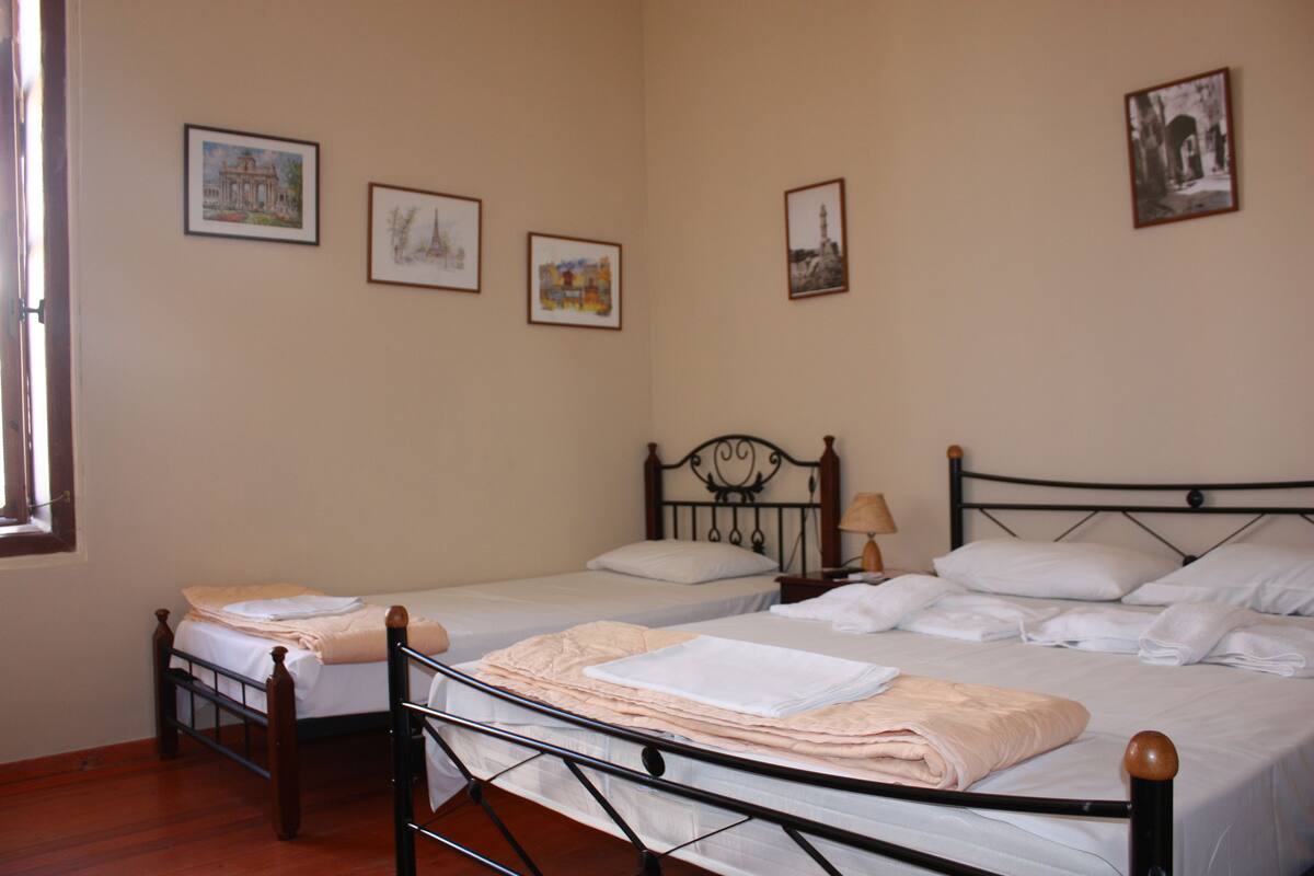Une chambre avec deux lits simples, un plancher en bois et quatre tableaux encadrés au mur.