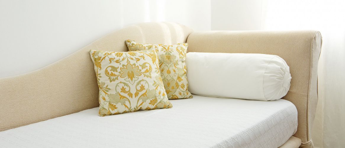 Ein beiges Sofa mit zwei gemusterten Kissen und einem schlichten weißen Kissen.