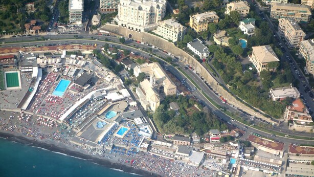 An aerial view of a coastal city with a densely populated beach area, a large hotel with a swimming pool, and a prominent building with a dome. - B&B Albaro (Genoa)