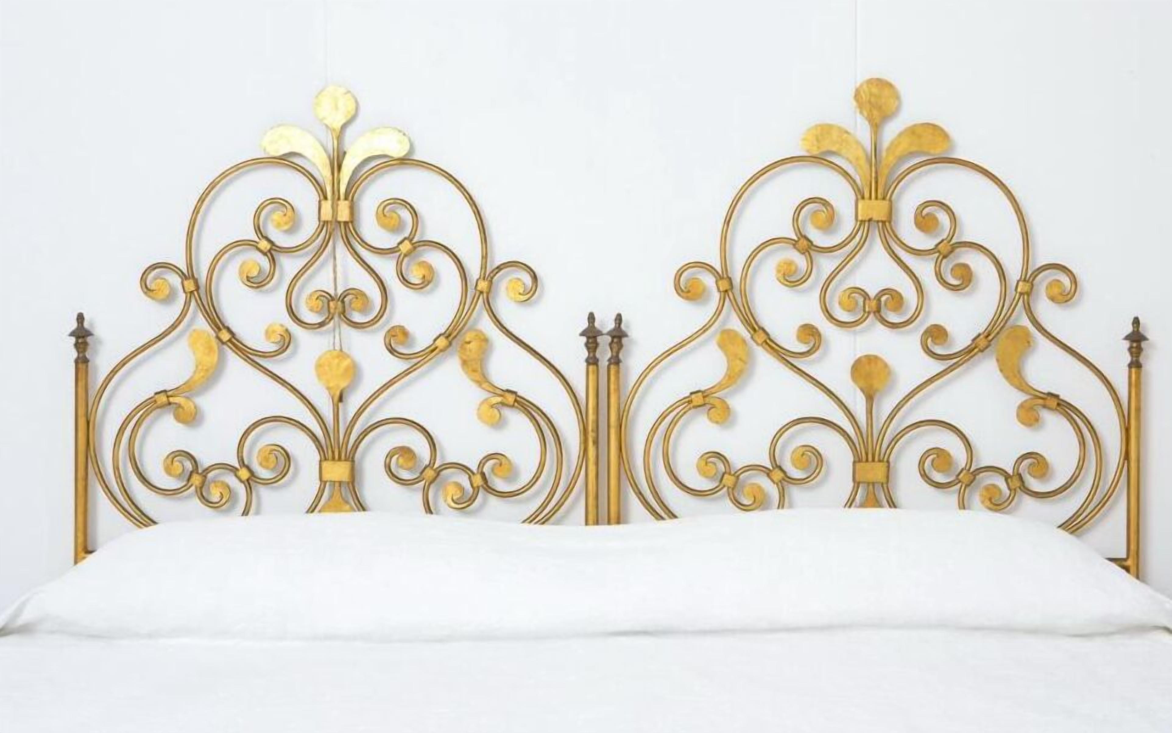 Een bed met een decoratief metalen hoofdbord met ingewikkelde versieringen en twee verticale stangen aan de uiteinden.