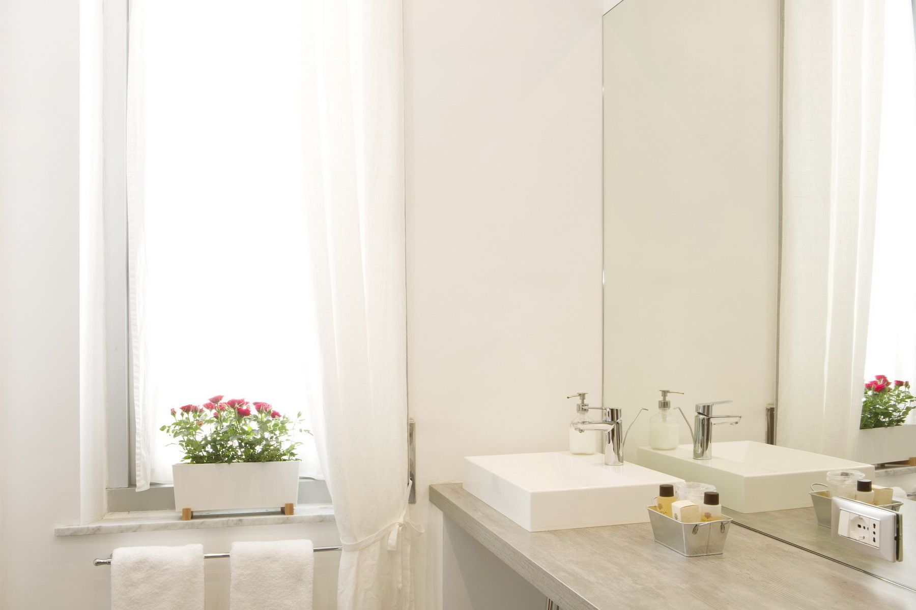 Een moderne badkamer met een grote spiegel, twee wastafels en een raam met een bloempot.