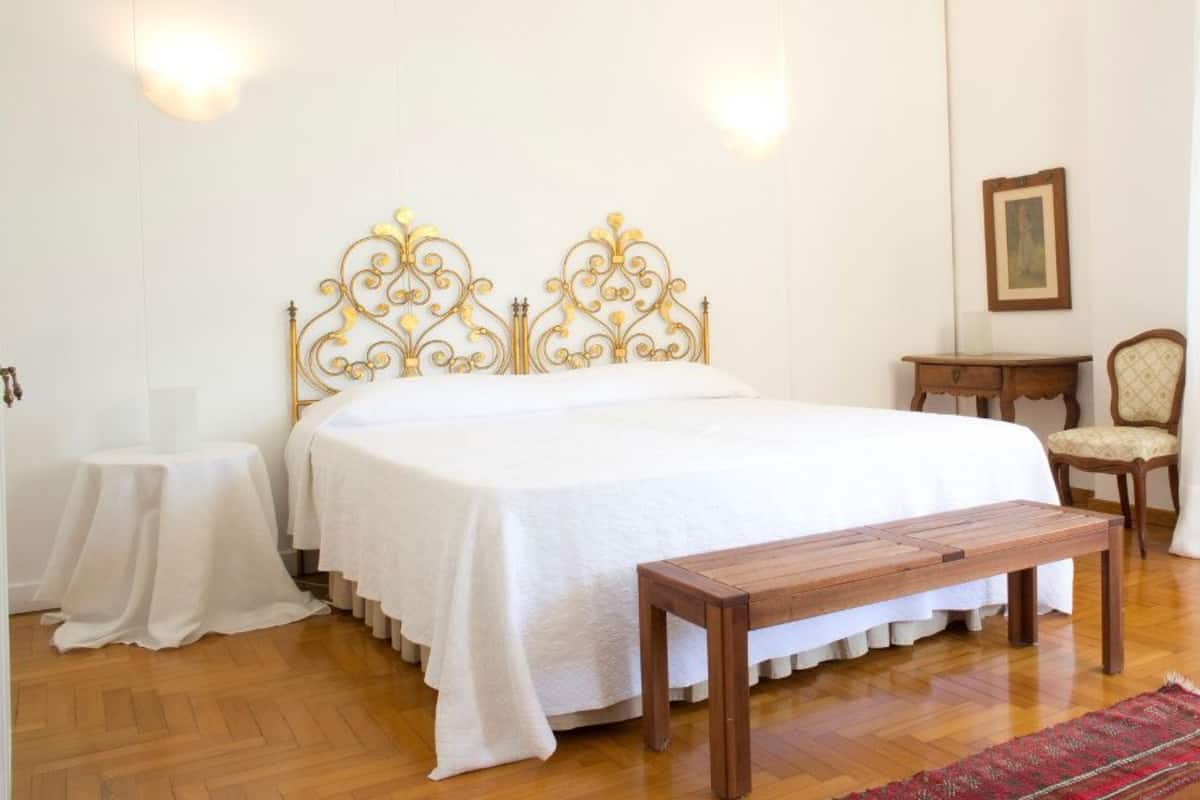 Un dormitorio con una cama grande, un banco de madera, una mesita y una silla.