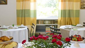 A dining area with two tables, each set with plates, cups, and a centerpiece of flowers. - B&B Albaro (Genoa)