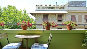 A balcony with two chairs and a small table, potted plants, and a building with decorative balconies in the background. - B&B Albaro (Genoa)