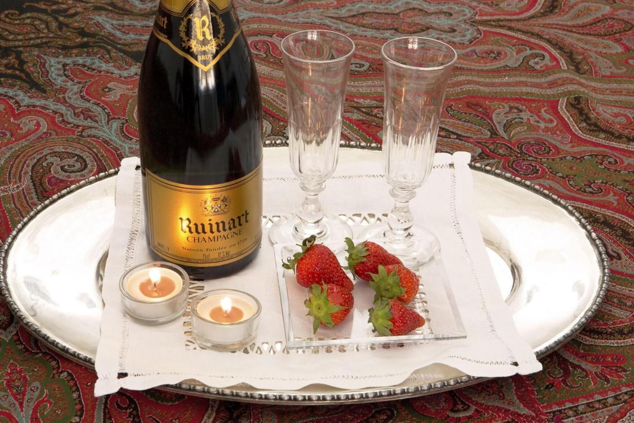 A bottle of Ruinart champagne, two glasses, strawberries, and candles on a tray.