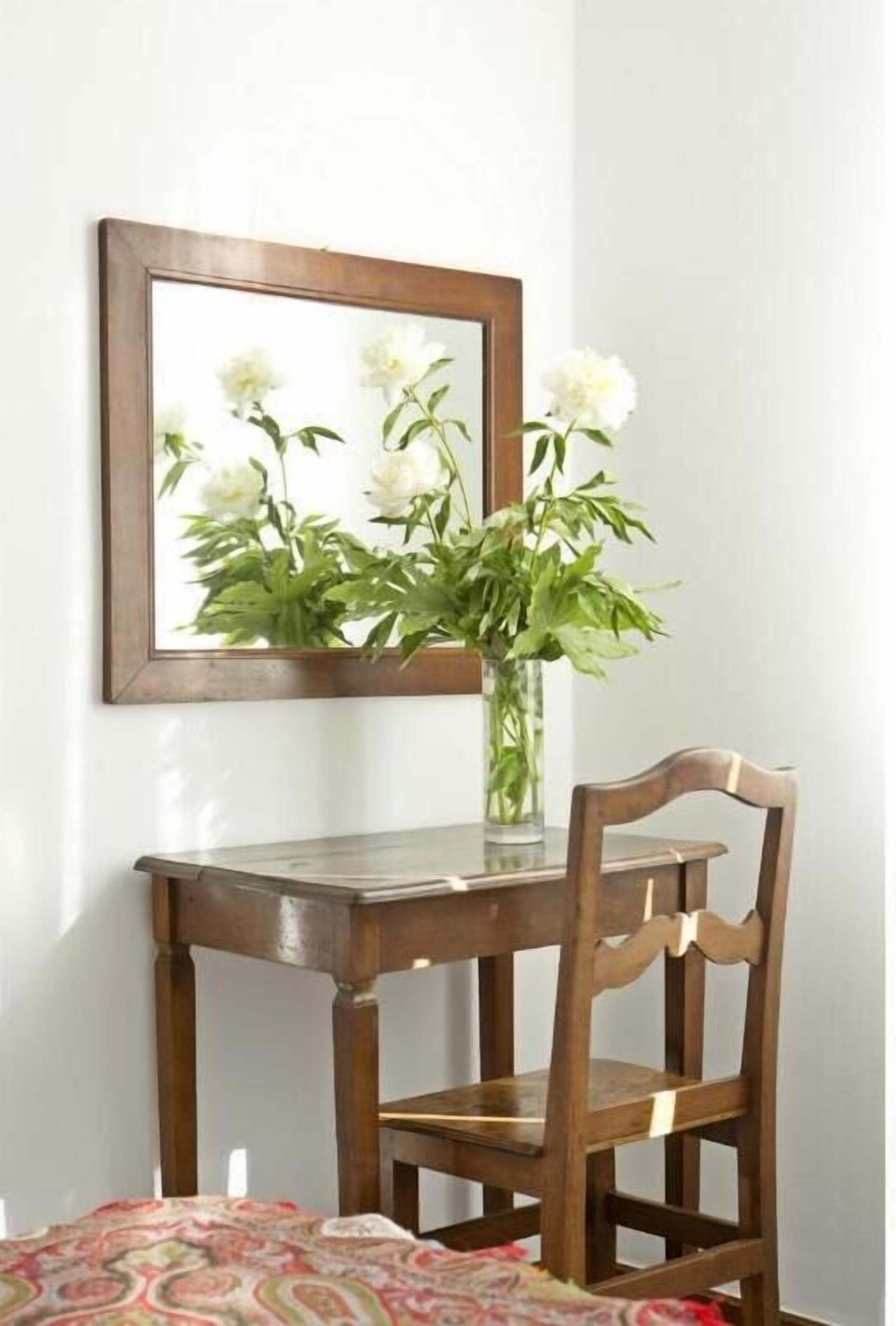 Una scrivania in legno con una sedia, un vaso con fiori bianchi e un quadro incorniciato appeso al muro.