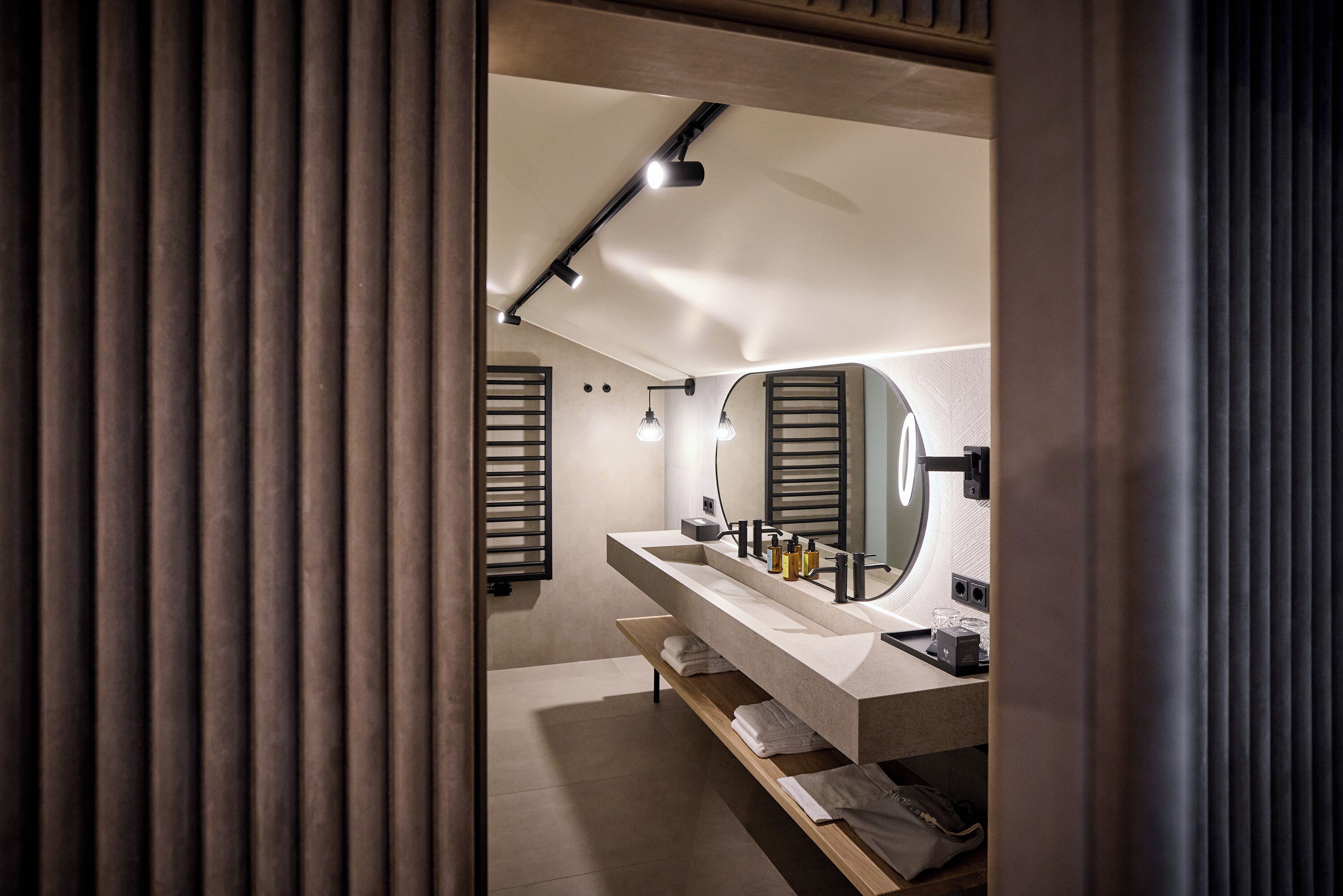 Ein modernes Badezimmer mit einem großen Spiegel, zwei Waschbecken und einem Ablagefach mit Handtüchern.