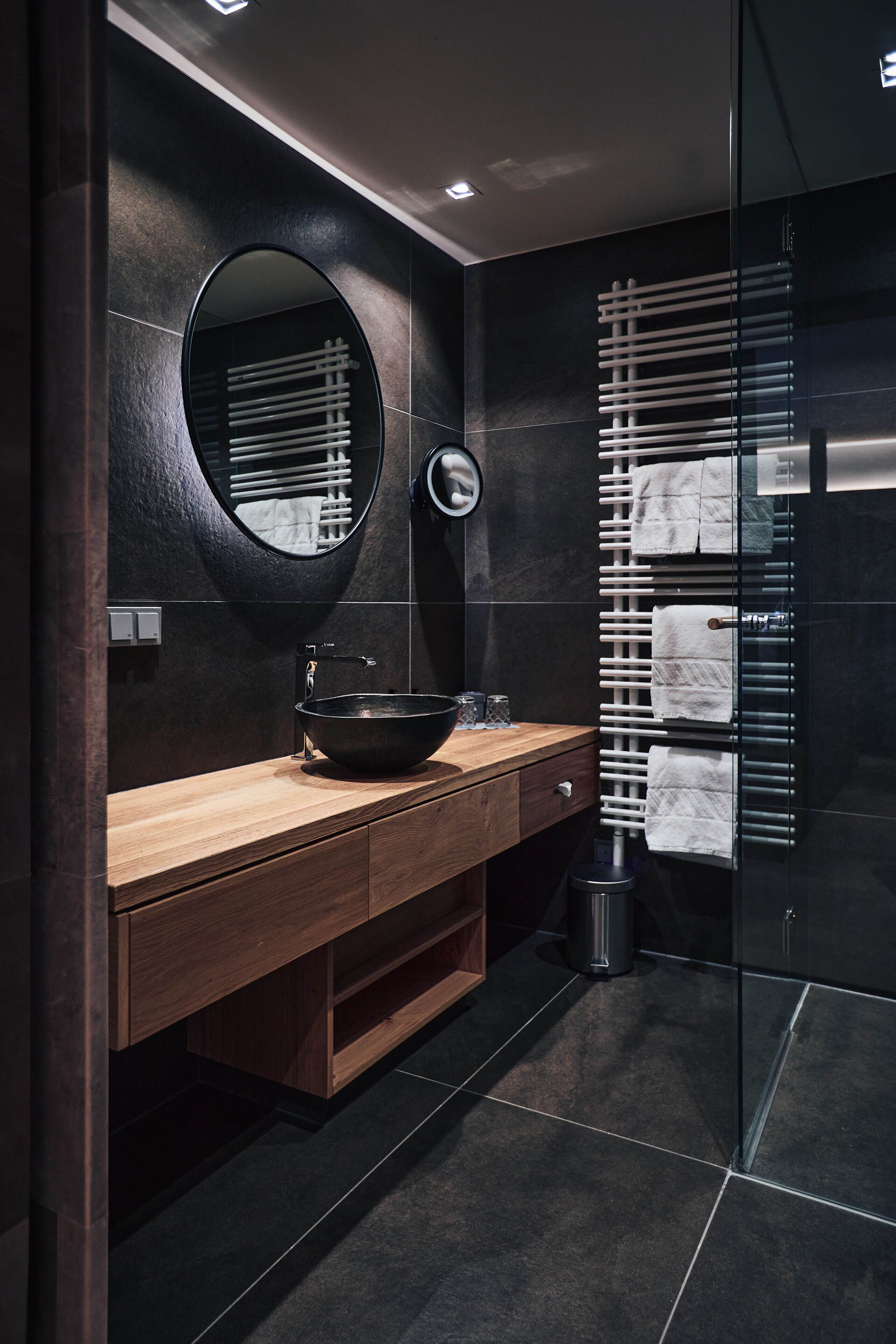 Une salle de bain moderne avec un meuble-lavabo en bois, un lavabo noir, un miroir rond et une cabine de douche en verre.