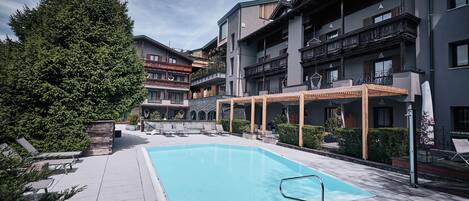 A swimming pool with lounge chairs, a pergola, and a large tree.