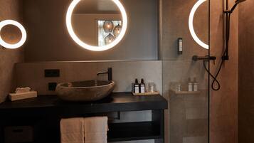 A modern bathroom with a large vessel sink, two illuminated mirrors, a glass shower enclosure, and a towel rack.