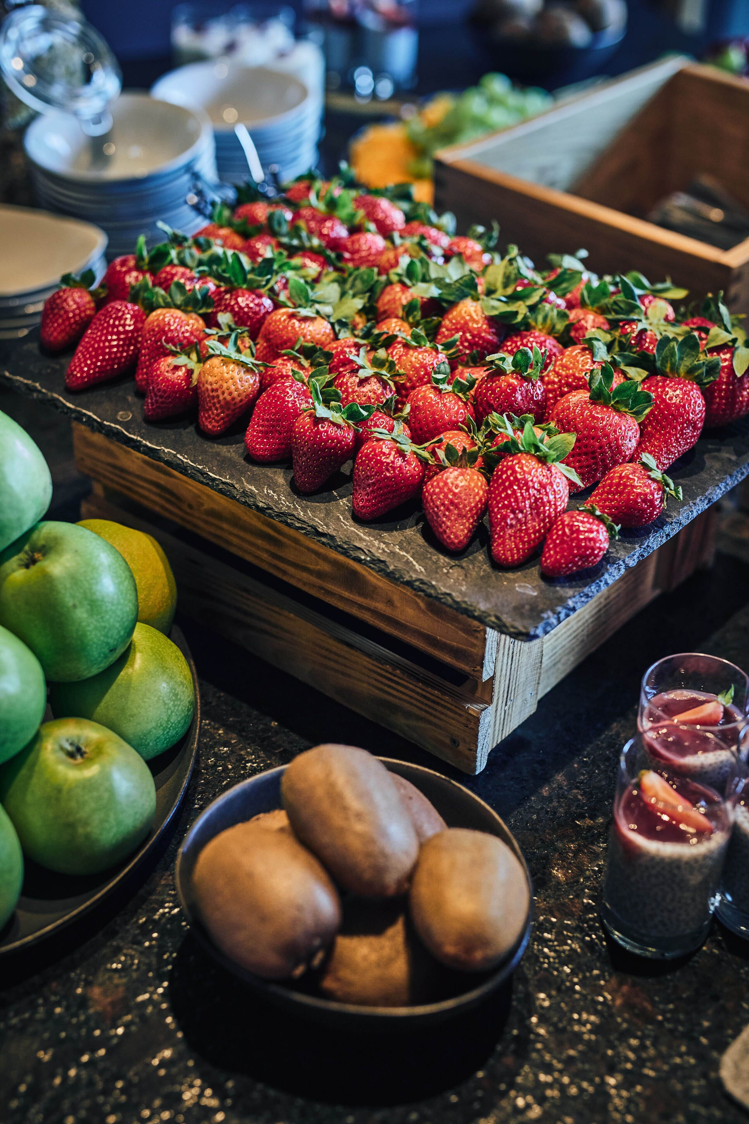 A buffet table with strawberries, apples, and kiwis.