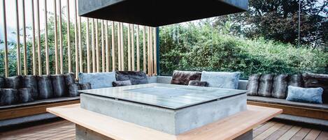 A modern outdoor seating area with a concrete table and wooden benches, surrounded by a wooden deck and bamboo fencing.