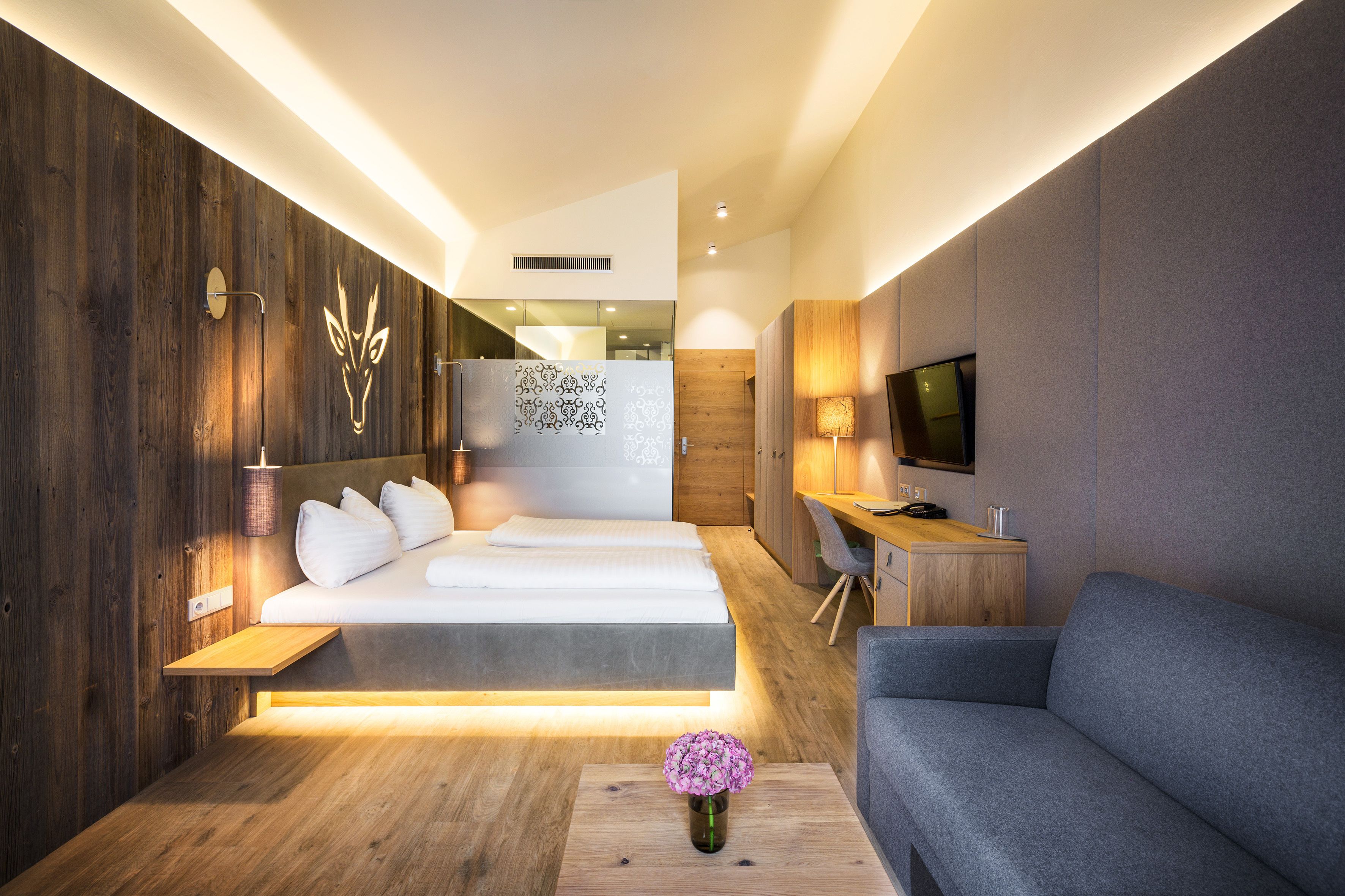 A modern hotel room with a bed, sofa, TV, and a small table with a vase.