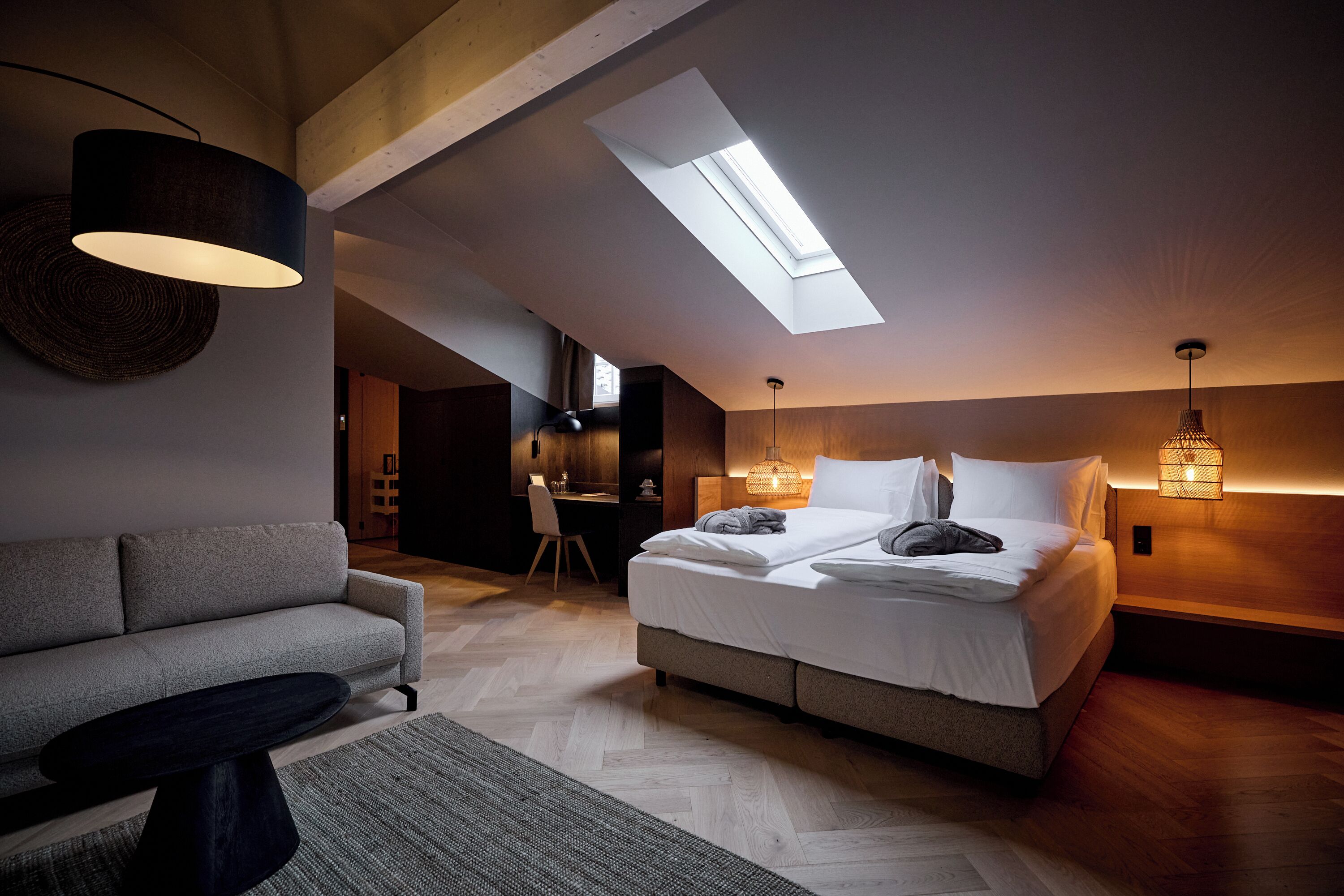 A modern bedroom with a skylight, a sofa, a desk, and a bed with a headboard.