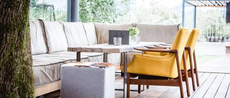 A modern outdoor seating area with a cushioned sofa, wooden chairs, and a small table with a vase of flowers.