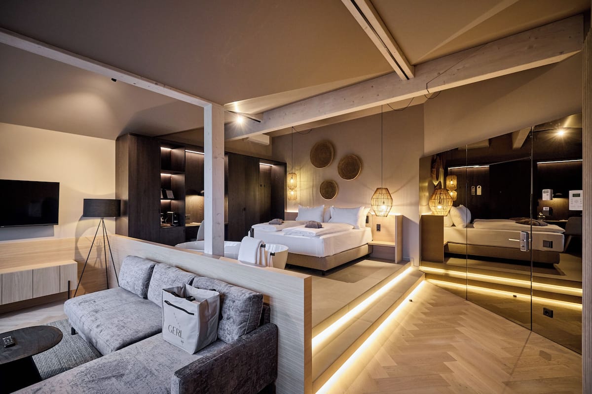 Una habitación de hotel moderna con una cama grande, un sofá, un televisor y un baño con espejo.