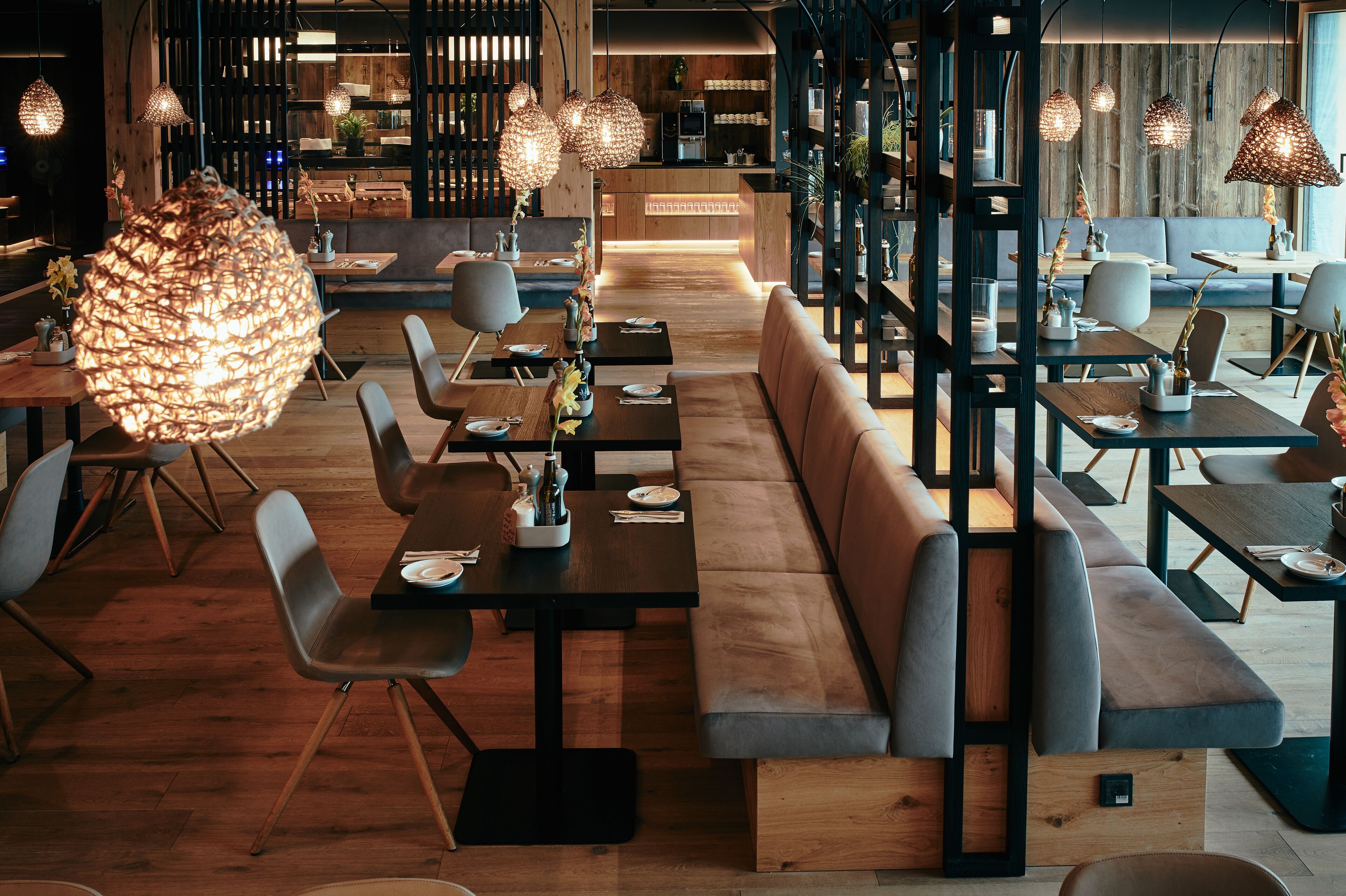 Et moderne restaurantmiljø med træborde, polstrede siddepladser og hængende lamper.