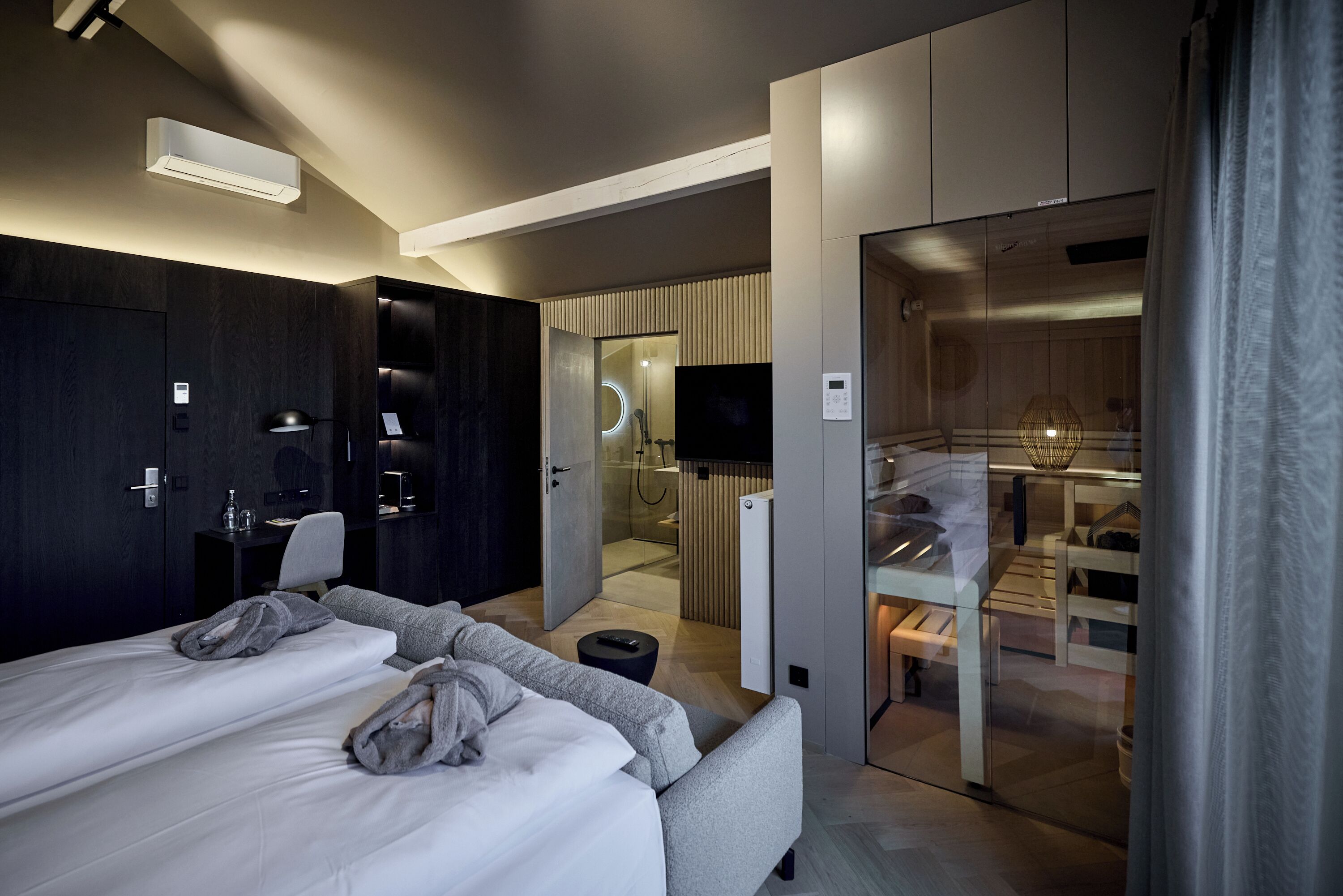 Een moderne hotelkamer met een bed, een bank, een bureau en een badkamer, zichtbaar door een geopende deur.