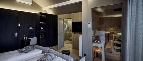 Een moderne hotelkamer met een bed, een bank, een bureau en een badkamer, zichtbaar door een geopende deur.