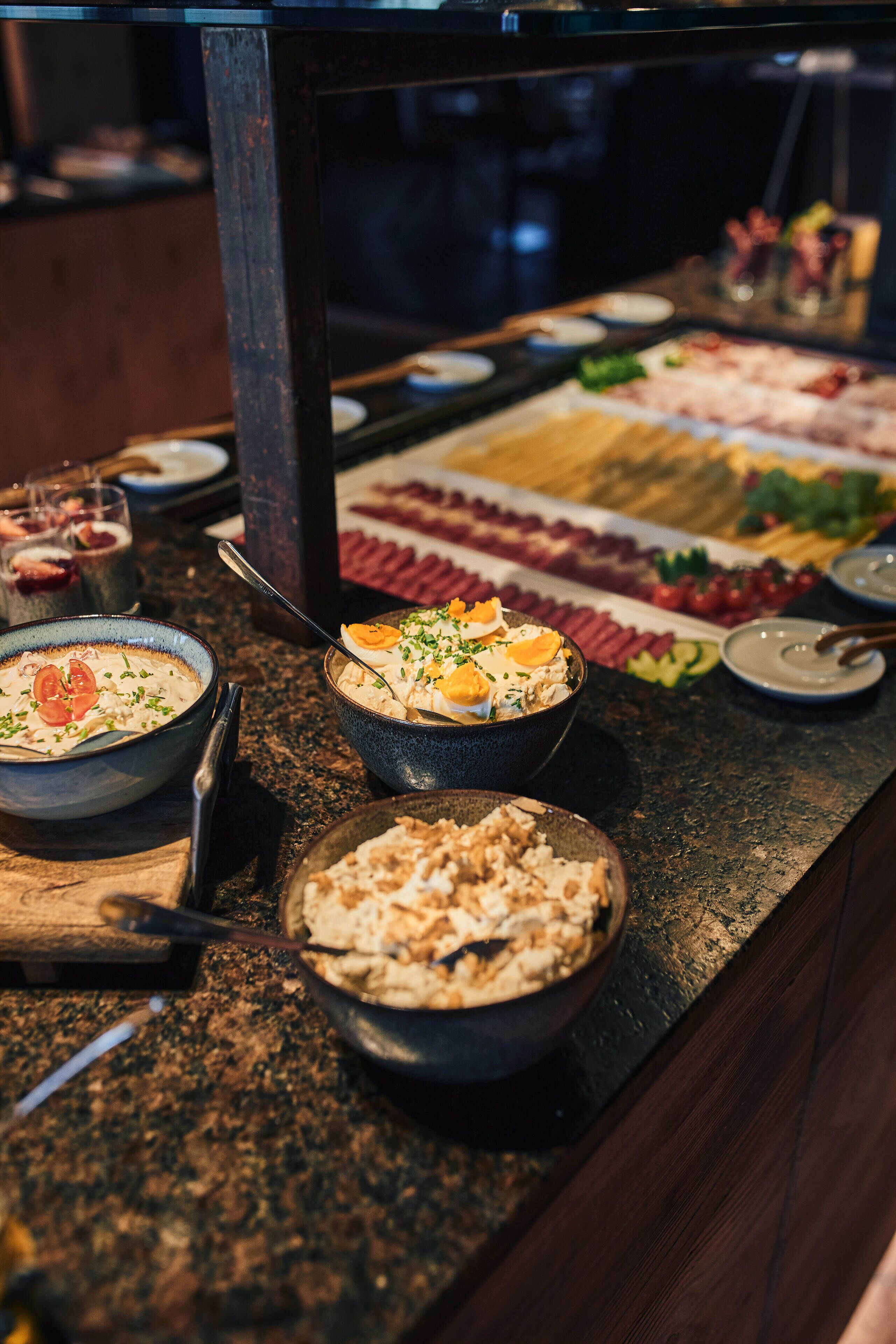A buffet with various dishes including a bowl of soup, a bowl of salad, and a plate of sliced meats.