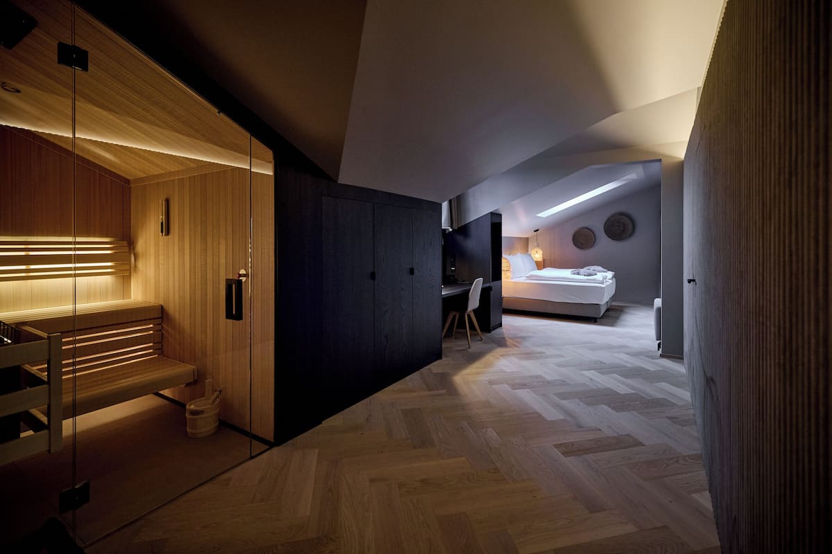 Una habitación de hotel moderna con un banco de madera, un escritorio, una cama y un suelo con estampado de espiga.