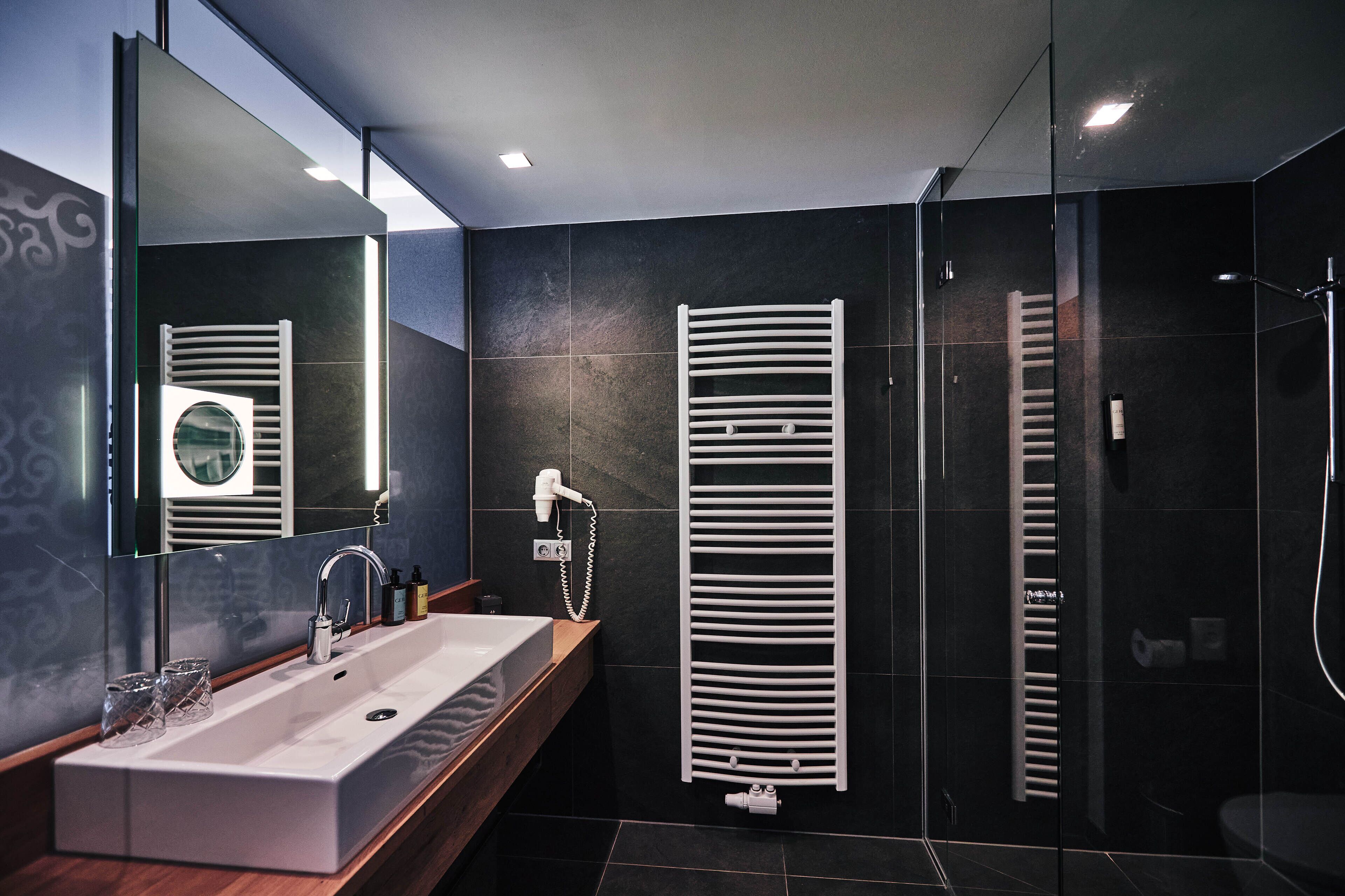 A modern bathroom with a large sink, a mirror, a towel rack, and a shower area.