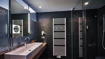 A modern bathroom with a large sink, a mirror, a towel rack, and a shower area.