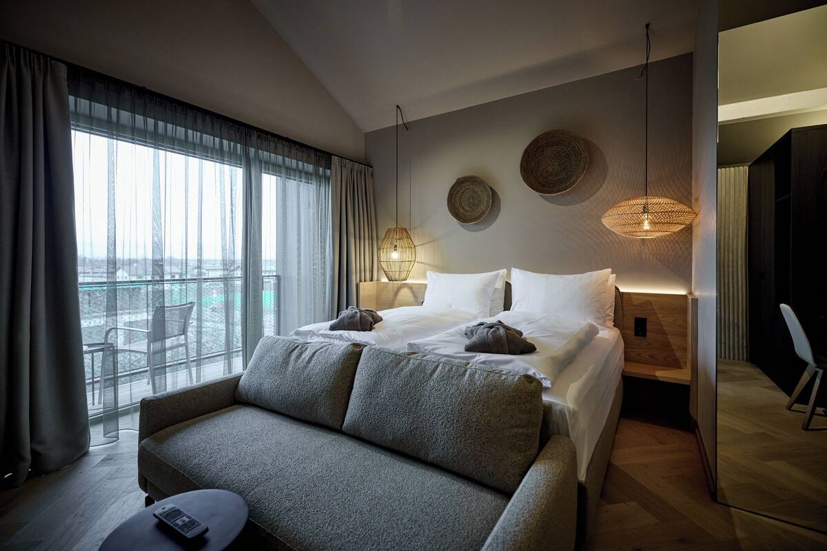 Una habitación de hotel moderna con una cama grande, un sofá, una mesita y vistas al balcón.