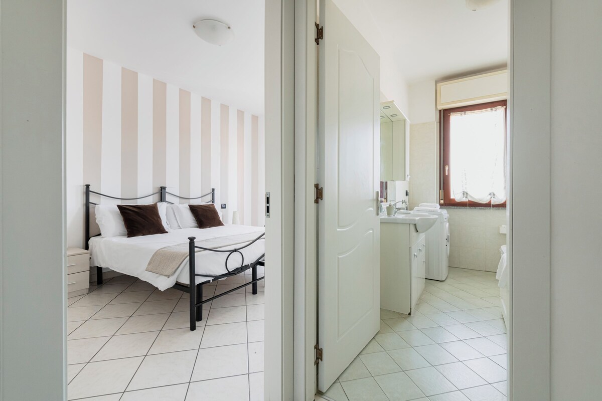 A bedroom with a bed, a bedside table, a wardrobe, and a bathroom with a sink and mirror.